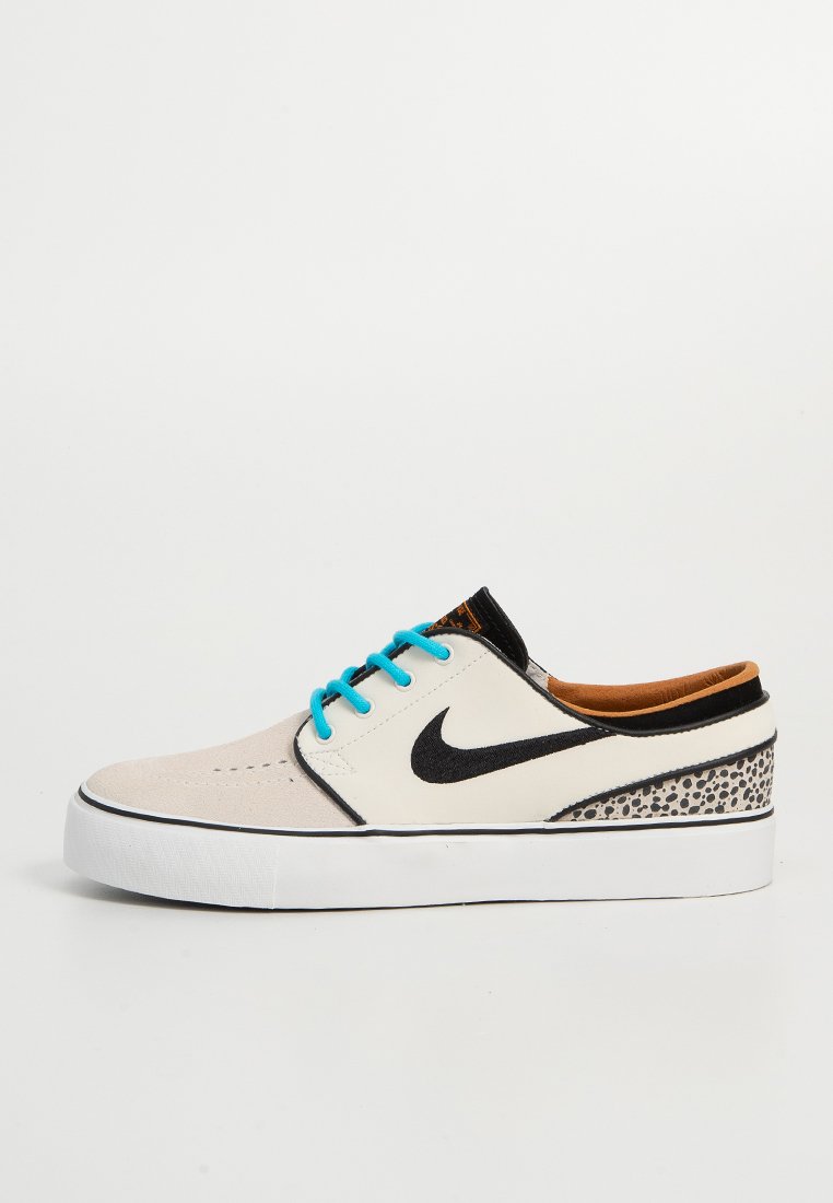 Zapatillas Nike con una parte superior de ante beige y sintético blanco, logo negro, cordones turquesa y una suela texturizada y con patrón.