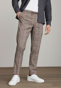 Brune ternede bukser med elastisk talje og snor, stylet med hvide sneakers. Stoffet har en let tekstur.