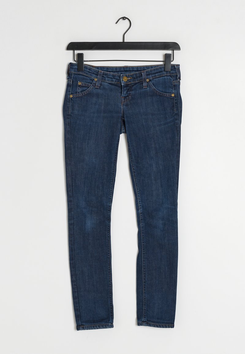 Jeans skinny en denim bleu foncé, avec une fermeture à glissière, cinq poches et des accents métalliques dorés. Texture lisse avec un léger délavage.