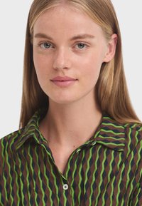 Kraagshirt met een geometrisch patroon in groen, marineblauw en bruin. Voorzien van een knoopsluiting en een lichte textuur.