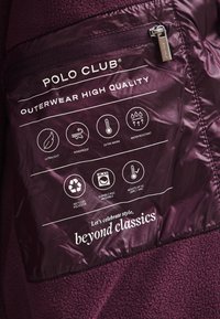 Vinröd fleecetröja insida med skötselråd och egenskaper: ultralätt, vindtät, varm, vattenavvisande, tillverkad av återvunnen polyester.