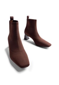 Botine maro, realizate dintr-un material elastic, cu vârf pătrat și tocul geometric. Designul include o parte superioară cu nervuri și o bucată pentru tras.