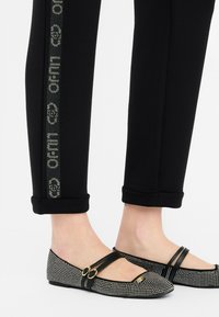 Zwarte taps toelopende broek met een patroon aan de zijkant, gecombineerd met zwarte flats met een rhinestonen ontwerp en twee bandjes.