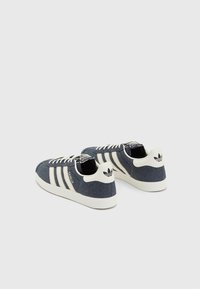 Blå denim sneakers med vita gummisulor, tre vita ränder och en logotyp på hälen. Har snörning och en strukturerad tygytan.