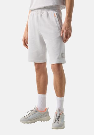 Mand iført lysegrå elastiske shorts med sidelommer, hvide crew-sokker og grå atletiksko med orange kant.