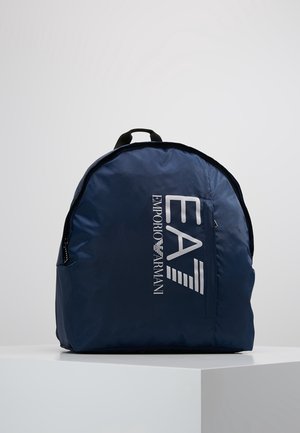 Marineblauer EA7 Emporio Armani Rucksack mit vorderer Reißverschlusstasche und schwarzem Griff, auf einem weißen Sockel vor grauem Hintergrund präsentiert.
