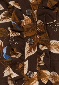 Brunt stof med et bladm�ønster i creme, guld og blå. Flæsekanter og sorte knapper udsmykker fronten.