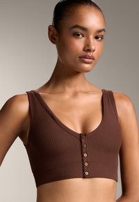 Bralette marron à côtes, avec un décolleté en V profond, des bretelles larges et une fermeture à boutons à l'avant. Sa texture lisse et son design ajusté améliorent le confort.