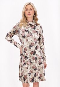 Kukallinen mekko pehmeästä, teksturoidusta kankaasta, jossa on pitkät hihat ja huppu kaula-aukko. Värit ovat beige, vaaleanpunainen ja musta, ja malli istuu rento.