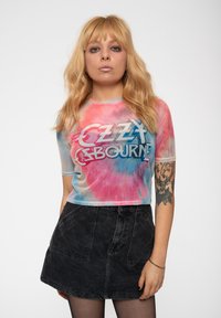 Tie-dye, short-sleeve top in pink and blue with text "OZZY OSBOURNE." Paired with a black denim skirt featuring front pockets and a fitted shape.