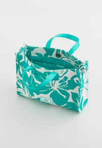 Turkisblomstret tote bag med hvide detaljer, der har to håndtag, en trykknapslukning og en blå indvendig del med en lomme.