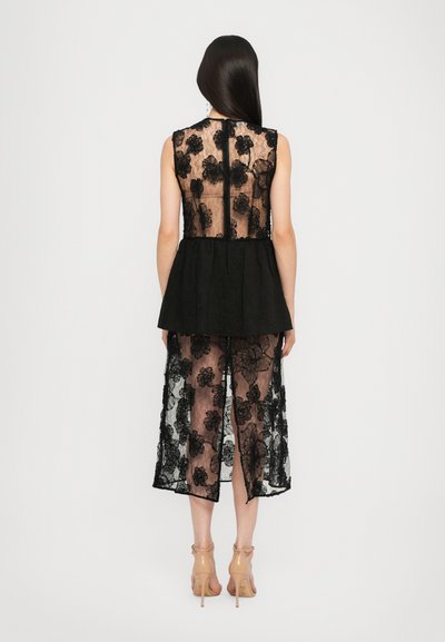 Vestido negro de encaje con bordados florales, espalda transparente y cintura de peplum negro. Presenta un superpón a la altura de la rodilla y cierre de cremallera en la parte trasera.