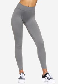 Leggings grigi alti in vita realizzati in tessuto elastico, con una texture liscia e una silhouette aderente, abbinati a sneakers nere e bianche.
