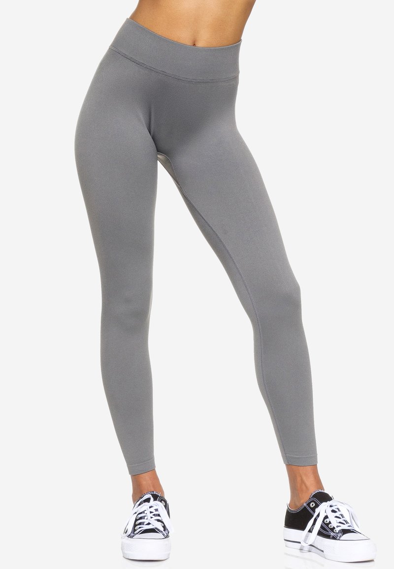 Leggings grigi alti in vita realizzati in tessuto elastico, con una texture liscia e una silhouette aderente, abbinati a sneakers nere e bianche.