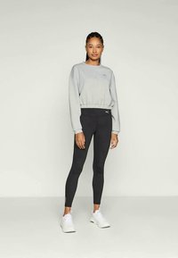 Sudadera gris recortada con dobladillo elástico, combinada con leggings negros ajustados que tienen un pequeño logo y zapatillas deportivas blancas.