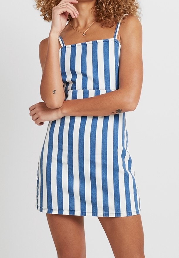Femme portant une mini-robe sans manches à fines rayures verticales bleu et blanc avec de fines bretelles et de petits tatouages sur les avant-bras.