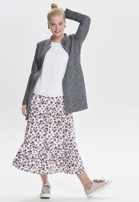 Giacca grigia e strutturata sopra una blusa bianca e una gonna a campana con motivo floreale in bianco, rosso e blu. Indossata con sneakers chiare.