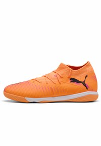 Orange fodboldsko med en struktureret, åndbar overdel, prydet med lyserøde detaljer og et sort logo. Slip-on design med lav profil.