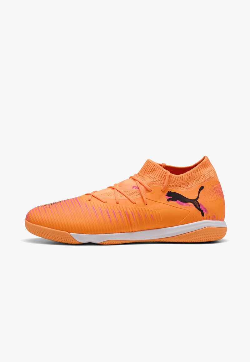 Orange fodboldsko med en struktureret, åndbar overdel, prydet med lyserøde detaljer og et sort logo. Slip-on design med lav profil.