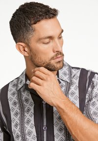 Camisa de manga corta con un tejido estampado en blanco y negro de diseño geométrico, cierre de botones y cuello doblado.