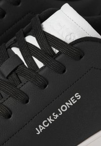 Sorte sneakers med en textured læderoverdel, sorte mesh-snører og et hvidt logo. Sålen er off-white, hvilket giver et to-farvet design.