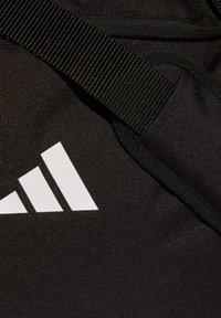 Bolsa de tela negra con superficie texturizada, un prominente logo blanco de tres rayas y una correa de nailon negra a juego.