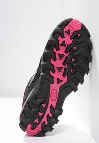 Trail running shoe sole in black rubber with prominent pink accents, featuring deep lugs for traction and a textured surface.