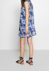 Abito senza maniche blu e bianco con stampa tie-dye, dal taglio morbido, abbinato a sandali espadrille neri con lacci alla caviglia.