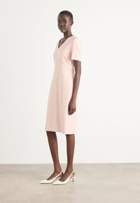 Knee-length, blush pink dress with short sleeves, V-neck, fitted design, and seam detailing, paired with white slingback heels.