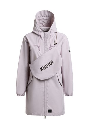 Kvinde iført en lysegrå hættetrøje, sorte leggings og sorte knælange støvler, stående foran en ensartet lysegrå baggrund.