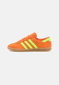 Orange suede sneakers with green accents, featuring three green stripes, a rubber sole, and a low profile design.