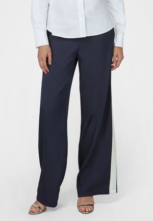 Woman wearing navy wide-leg pants with white side stripes and silver open-toe sandals, paired with a white button-up shirt.