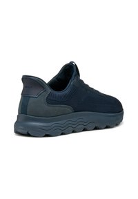 Zapatilla deportiva azul marino con parte superior de malla y acentos de ante suave. Cuenta con una suela gruesa y ondulada para mayor amortiguación y un collar acolchado.
