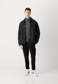 Svart knappet jakke, grå høyhalset genser, svarte cargo-bukser og hvite joggesko med svarte detaljer. Glatt tekstur, uformelt design.