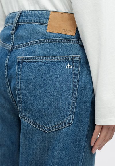 Közepesen kék színű farmernadrág bőrbélyegzővel a hátsó zsebén, amelyen a "rag & bone" márkanév látható. Egyenes szárú kialakítás.