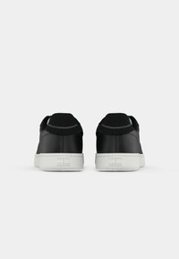 Een paar zwarte sneakers met witte zolen, weergegeven vanuit de achterkant met "Tommy Jeans" branding op de hak van elke schoen.