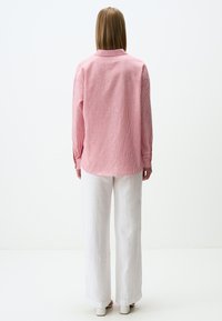 Rot-weiße gestreifte Bluse mit langen Ärmeln, Kragen und lockerer Passform, kombiniert mit weißen, weiten Hosen. Einfaches Design, keine Muster.