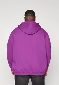 Violetti huppari, jossa nyörillä kiristettävä huppu, valmistettu pehmeästä kankaasta, rento malli ja resorit hihoissa sekä helmassa. Yksivärinen, ilman kuvioita.