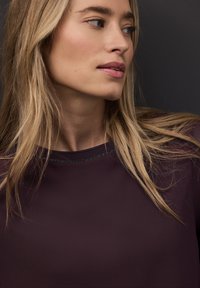 Jersey de tejido morado intenso con una textura suave. Presenta un escote redondo con un sutil detalle de hilo metálico.