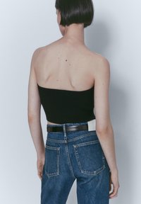 Haut court bandeau côtelé noir associé à un jean en denim bleu taille haute. La tenue comprend une ceinture noire et des poches arrière visibles.