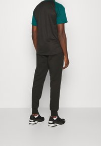 Černé sportovní kalhoty v kombinaci s černým a tyrkysovým tričkem s krátkým rukávem, vyrobené z hladkého, elastického materiálu. Černé tenisky s bílými detaily.