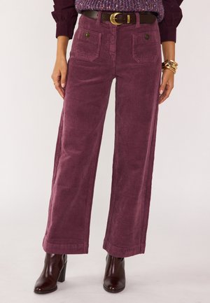 Pantaloni a gamba larga in corduroy viola con tasche frontali, vita alta e finitura testurizzata, abbinati a stivaletti con tacco marroni.