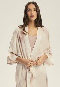 Lekki, kremowy szlafrok w kwiatowy wzór, z szerokimi rękawami i zawiązywany w talii; noszony na cielistej koszulce.