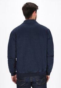 Tengerész bomberdzseki textúrált anyagból, bordás alsó szegéllyel és gallérral, egyszerű dizájnnal, látható díszítések nélkül.