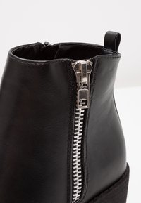 Stivaletto in pelle nera con cerniera argentata laterale, superficie testurizzata e un leggero tacco a zeppa.
