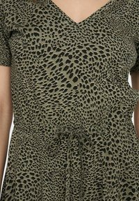 Olivengrünes Kleid mit kurzen Ärmeln, V-Ausschnitt und schwarzem Tupfenmuster. Verfügt über einen Kordelzug in der Taille für eine verstellbare Passform.