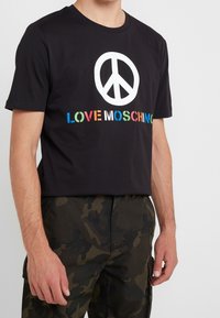 Zwart katoenen T-shirt met een groot wit vredessymbool en "LOVE MOSCHINO" in meerkleurige letters. Korte mouwen en ronde hals.