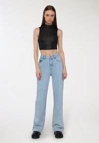 Czarny bezrękawnik z wysokim dekoltem, w połączeniu z jasnoniebieskimi spodniami z wysokim stanem i szerokimi nogawkami oraz ciężkimi, czarnymi platformami.