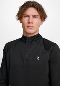 Zwarte quarter-zip pullover van textuurstof, voorzien van een klein chevronlogo op de borst. Staande kraag en een aansluitend ontwerp.