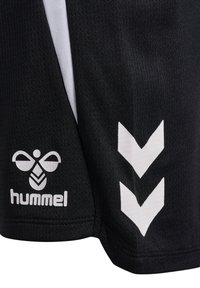 Schwarze Sportshorts mit weißen Chevron-Mustern und einem stilisierten Bienen-Logo über dem Schriftzug "hummel" auf strukturiertem Stoff.